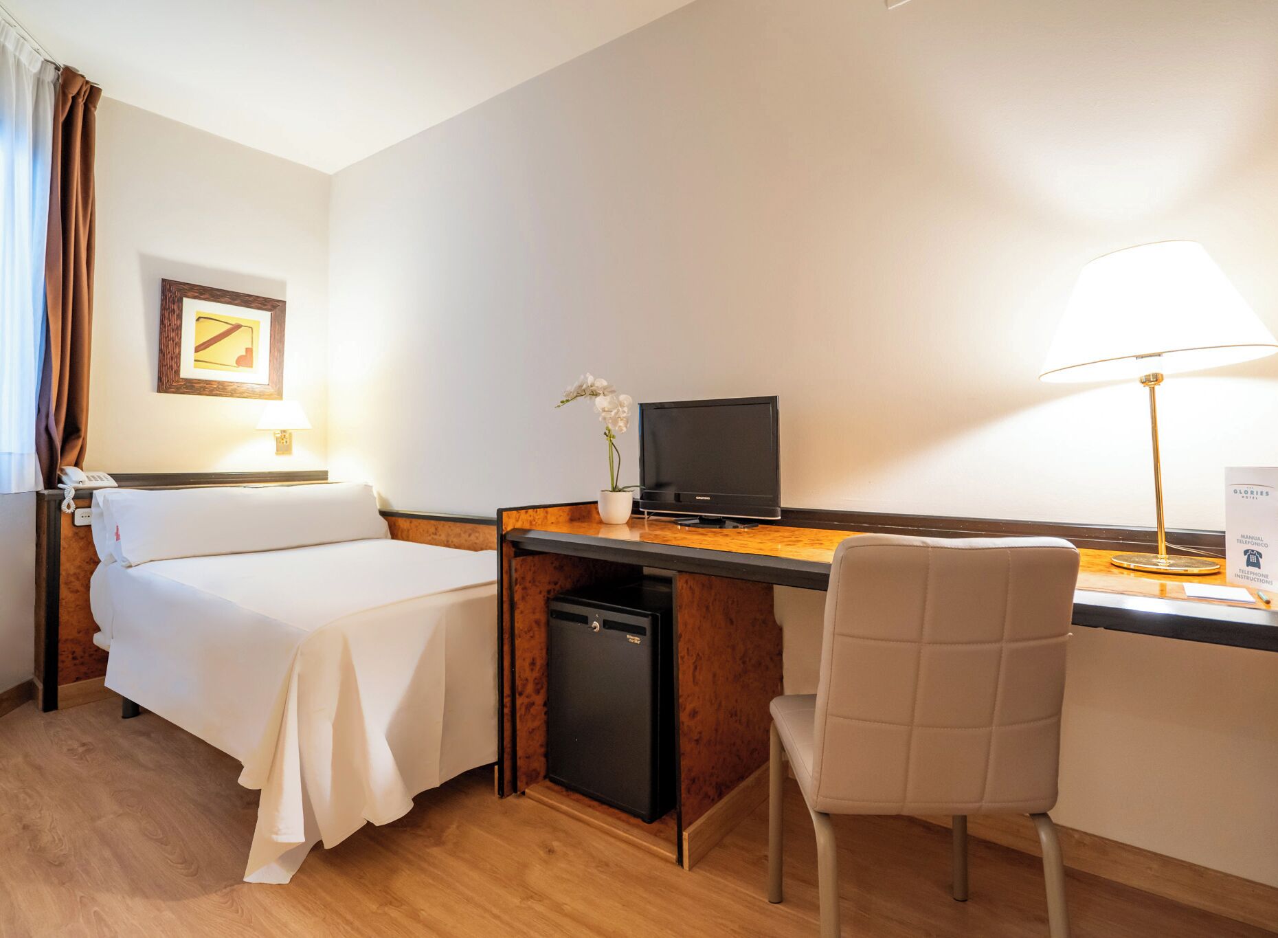 A hotel room with two beds, a desk with a computer, a chair, a lamp, and a small potted plant.