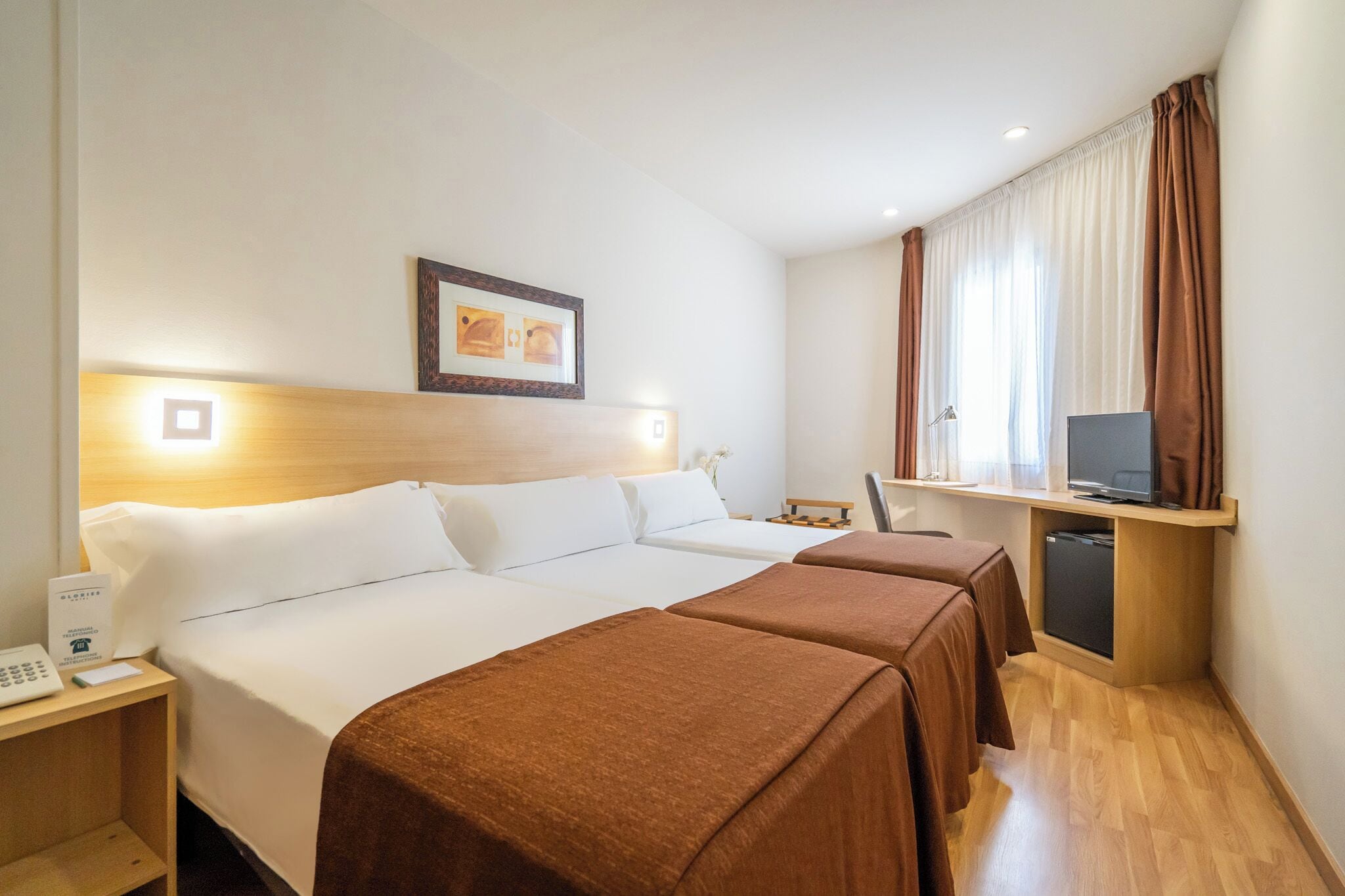 A hotel room with two beds, a desk with a computer, a TV, and a small fridge.