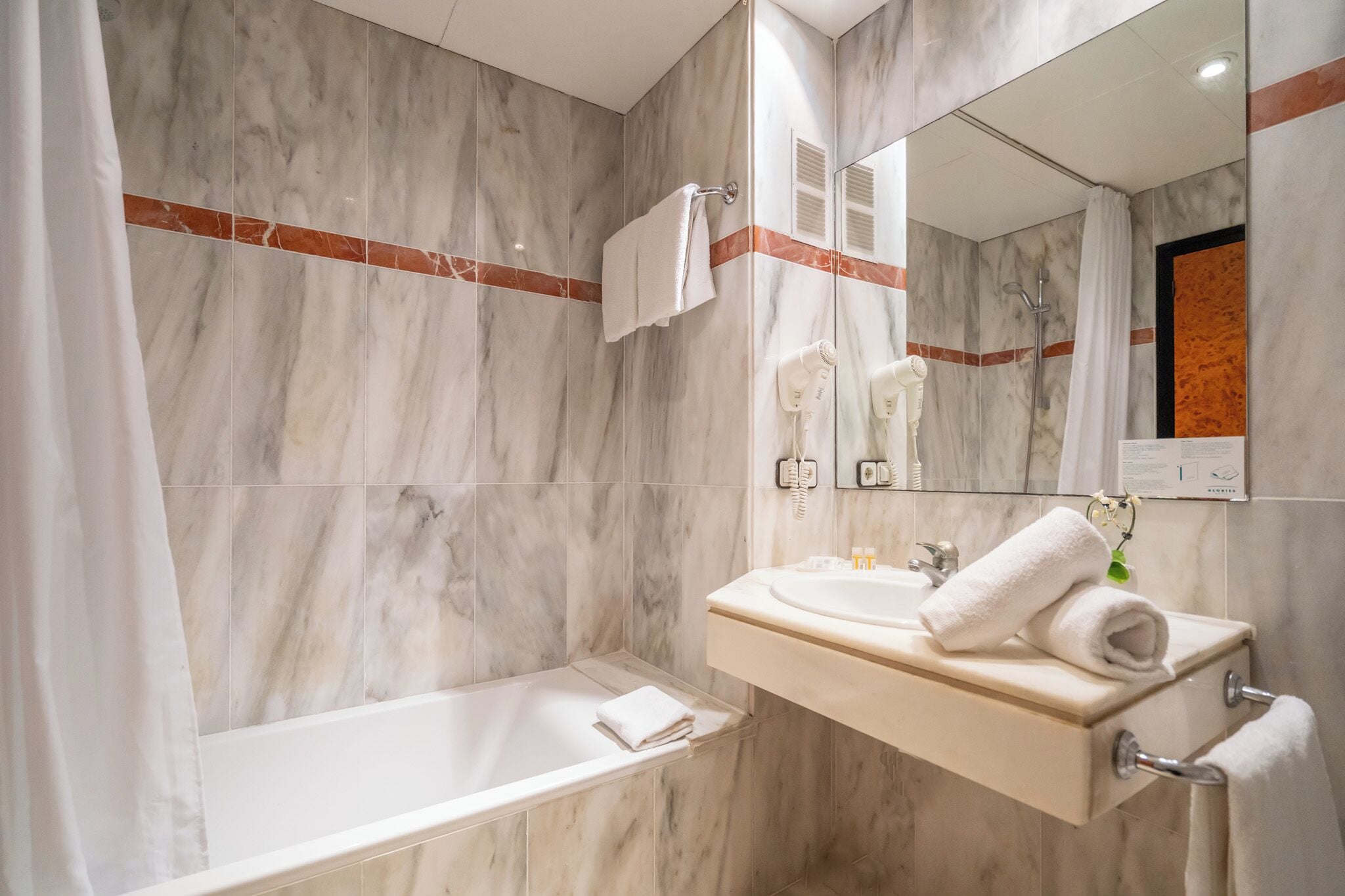 Une salle de bain moderne avec un mur en marbre, une baignoire, un lavabo avec une serviette et un miroir.