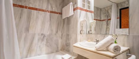 Un baño moderno con pared de mármol, una bañera, un lavamanos con una toalla y un espejo.