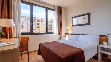 Een hotelkamer met een groot raam, een bed, een bureau en een stoel.
