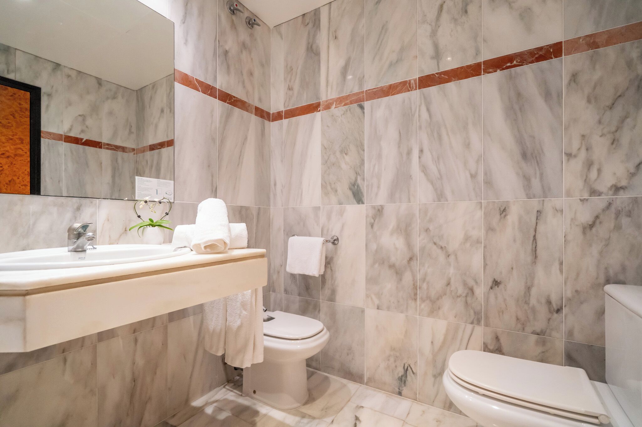 Un bany amb paret de marbre, un lavabo, una tassa i un mirall.