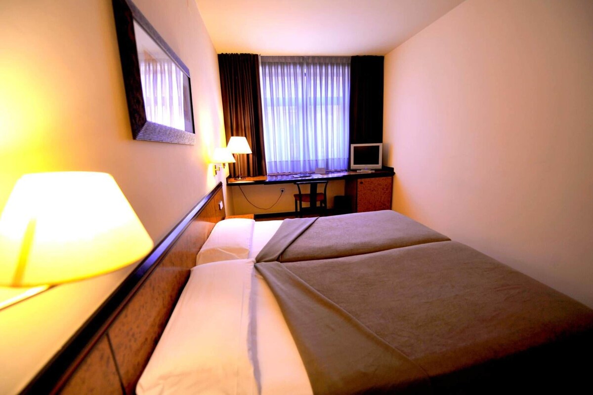 Una camera d'albergo con un letto, una scrivania, una televisione e una lampada.