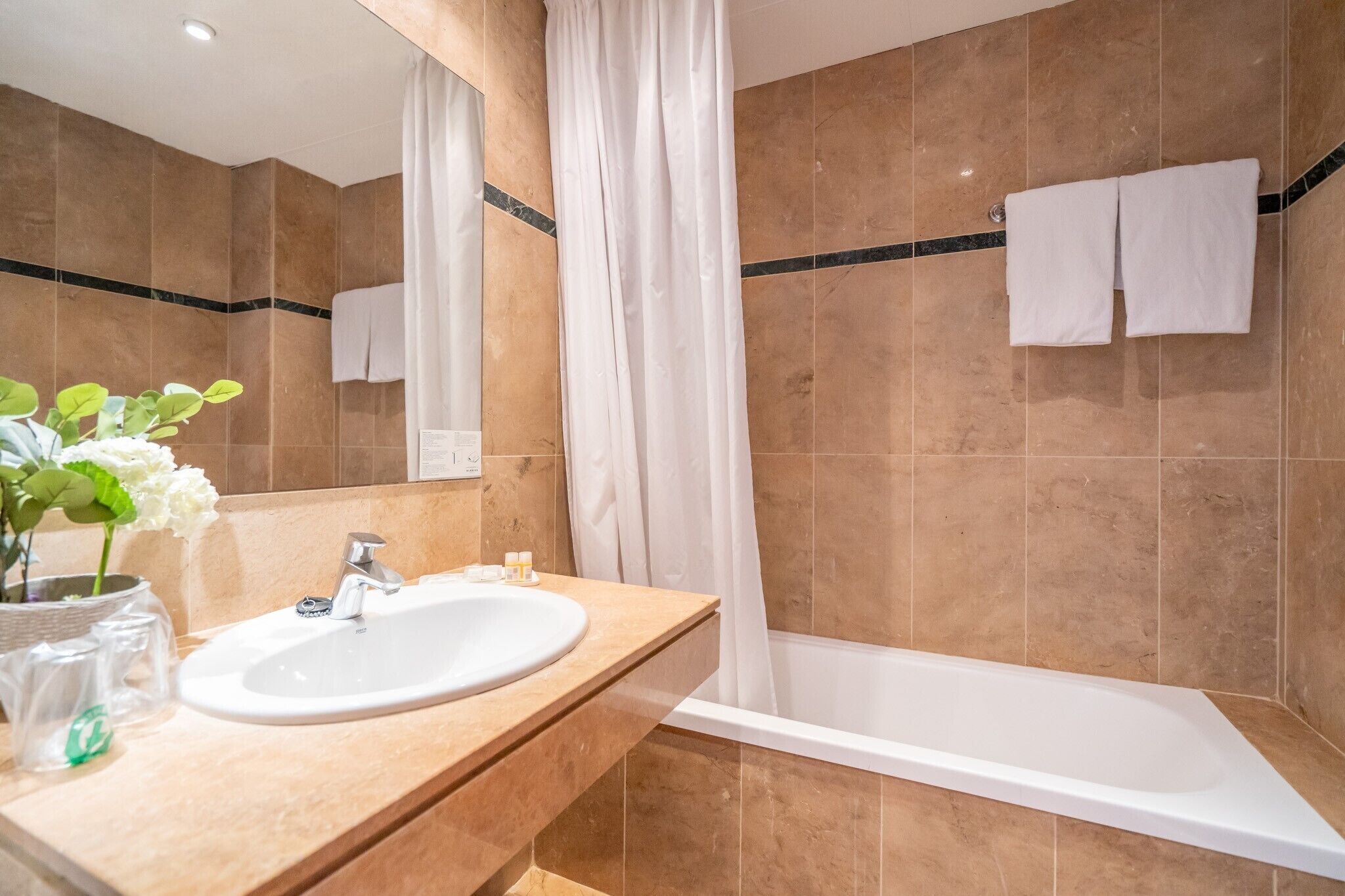 A bathroom with a sink, mirror, and bathtub.