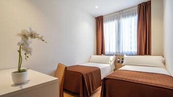 Habitación de hotel con dos camas, una mesita con una orquídea en maceta y una ventana con cortinas.