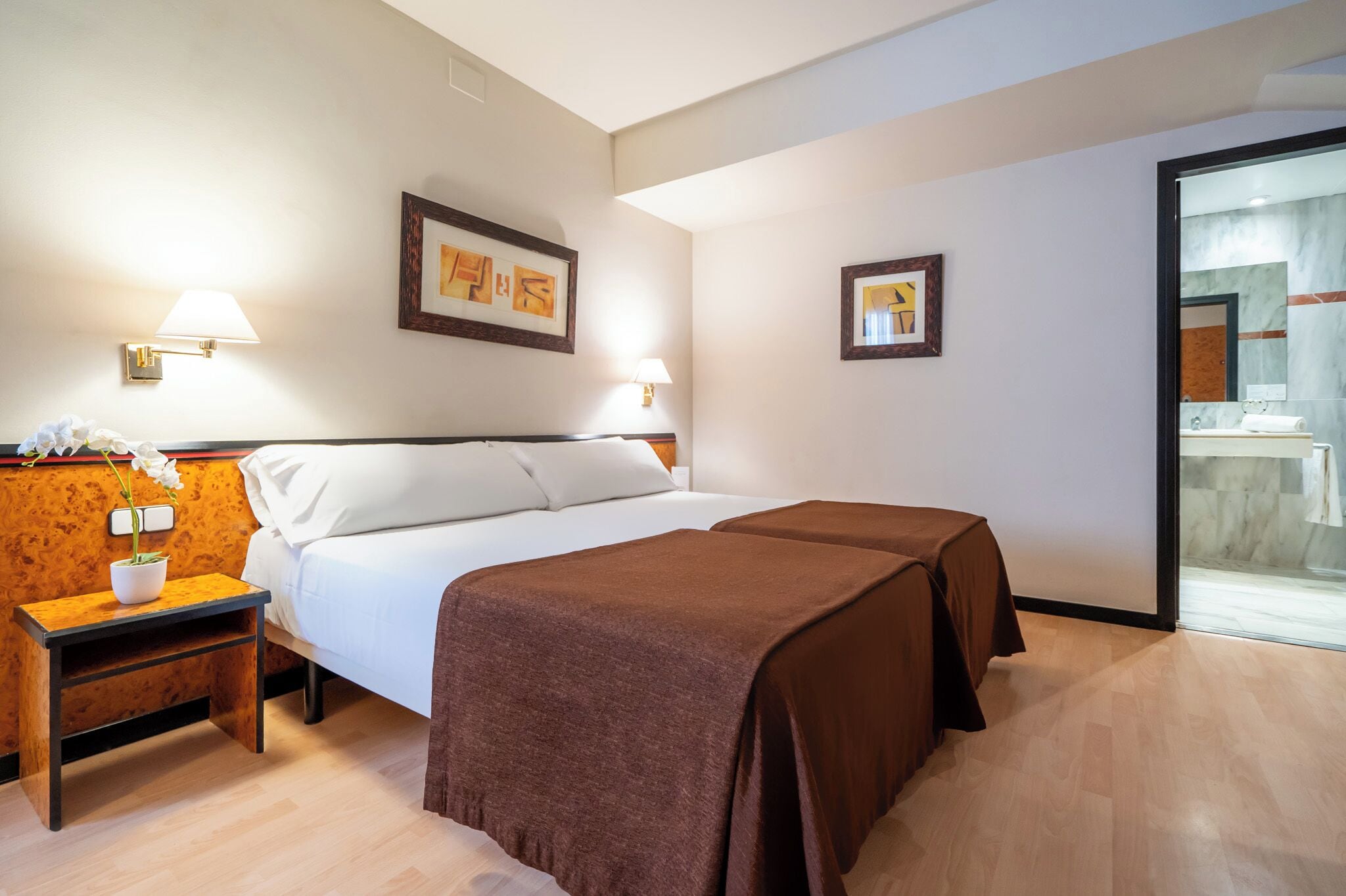 A hotel room with a bed, two bedside tables, a nightstand, and a large window.