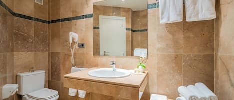 A bathroom with a toilet, sink, mirror, towels, and a hairdryer.