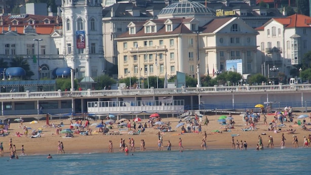 A beach with people and umbrellas, a hotel named "HOTEL HOVIELA" in the background, and a white building with a dome. - Hotel Hoyuela (Santander)