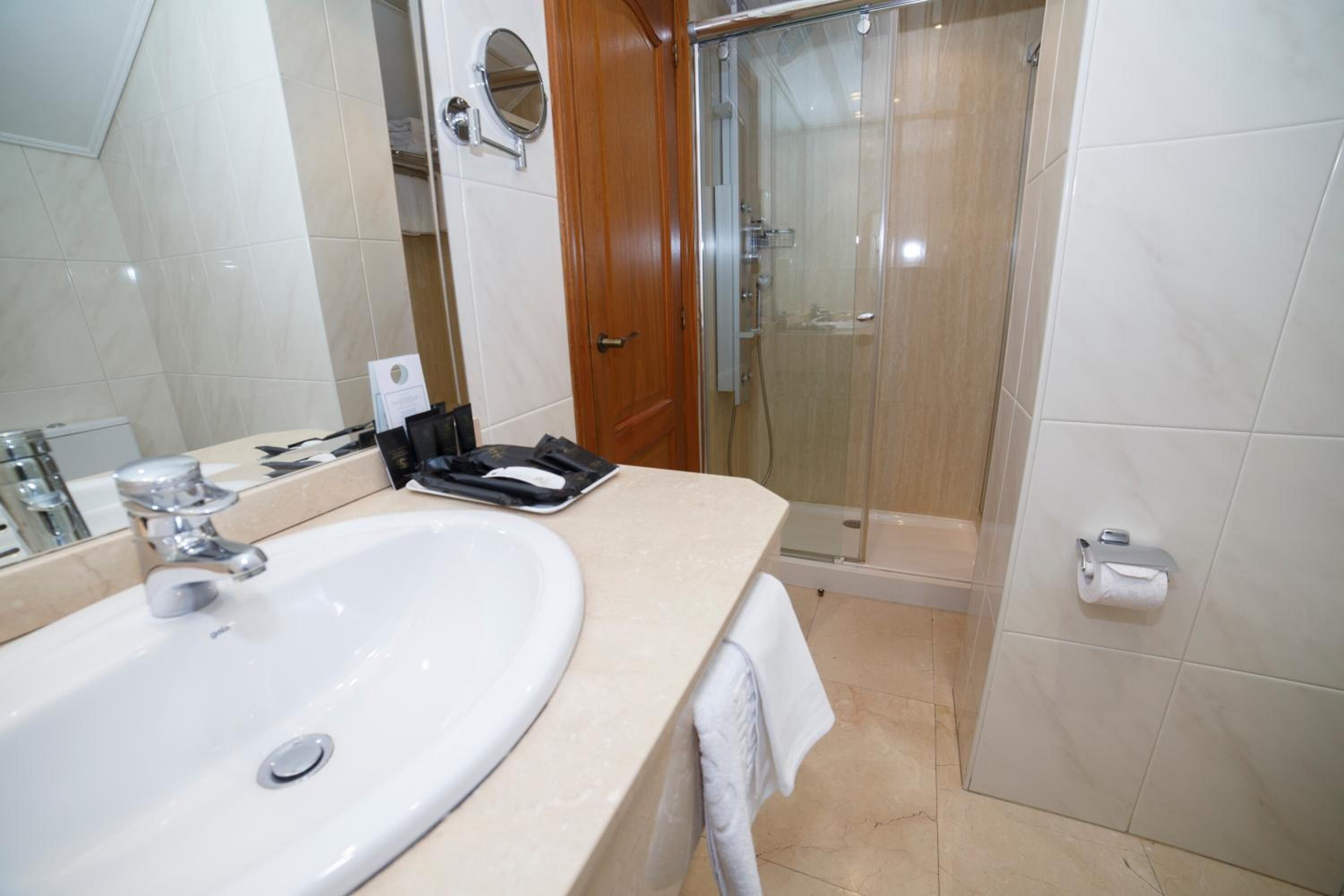 Un baño con un lavamanos blanco, un espejo, una toalla y una cabina de ducha de vidrio.