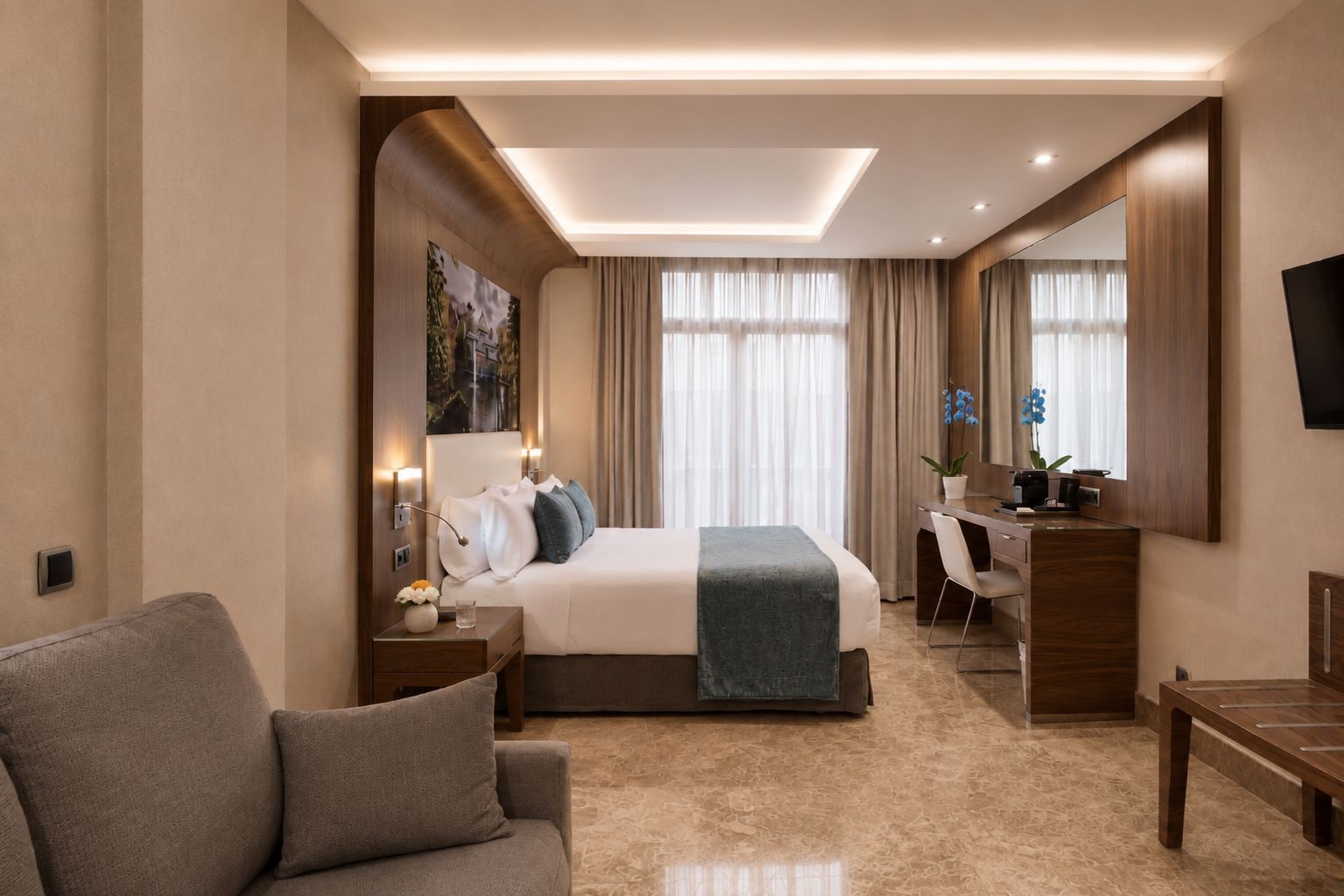 A hotel room with a bed, a desk, a chair, a sofa, and a TV.