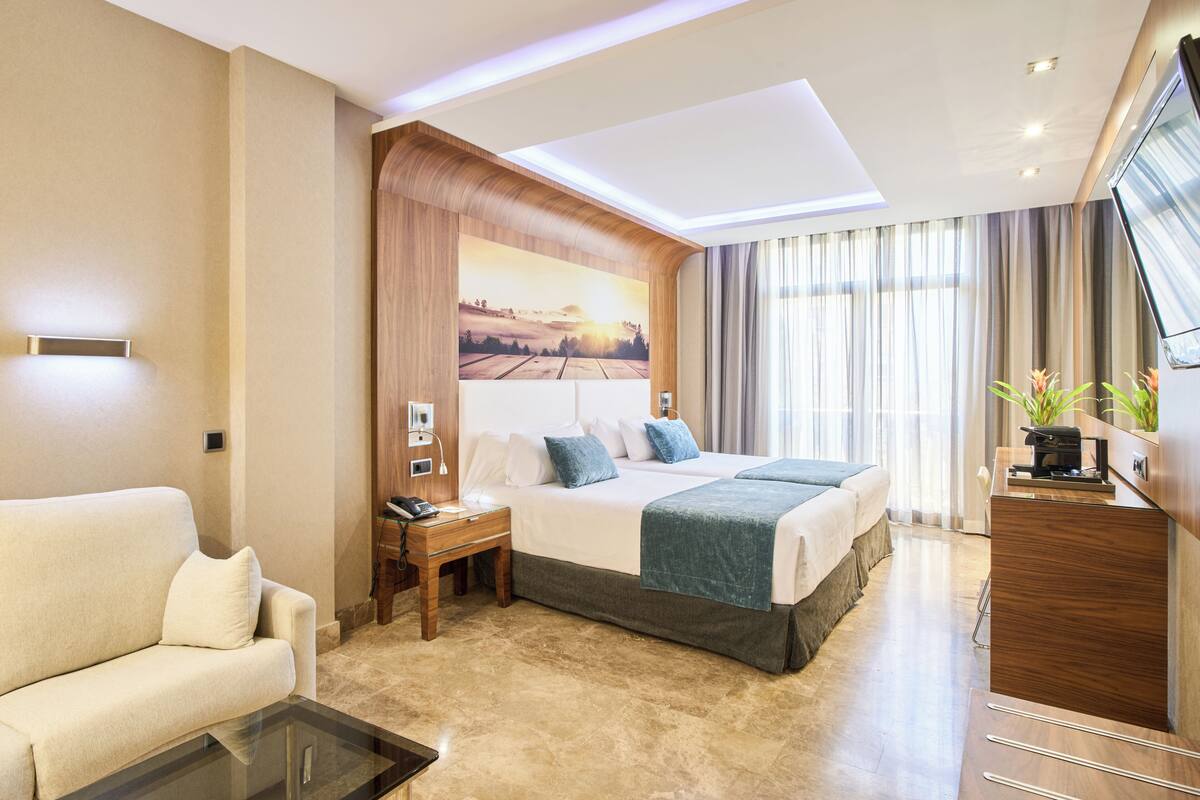 Ein modernes Hotelzimmer mit einem großen Bett, einer Couch, einem Schreibtisch und einem Fernseher.
