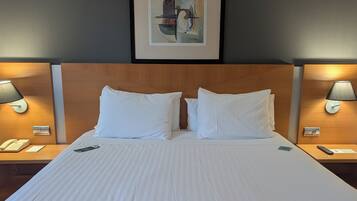 Habitación de hotel con una cama grande, dos lámparas de noche, una obra de arte enmarcada sobre la cama y un cabecero de madera.