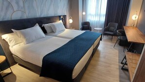 Ein Hotelzimmer mit einem großen Bett, zwei Nachttischen, einem Schreibtisch und einem Sessel.
