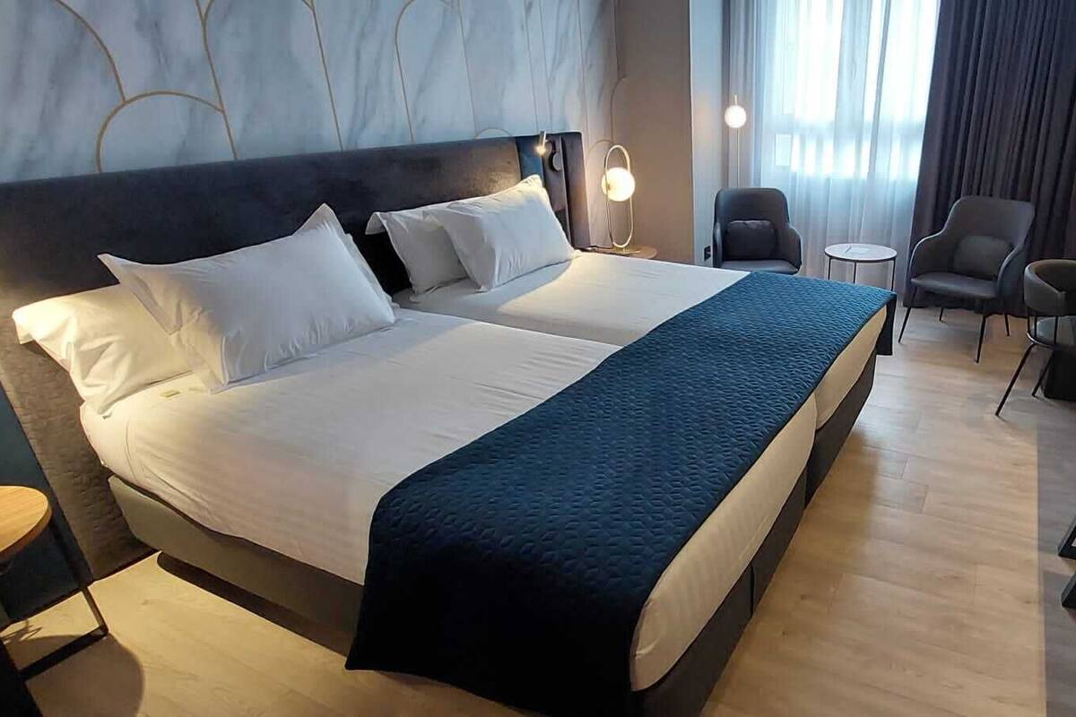 Una habitación de hotel con una cama grande, dos mesitas de noche, un escritorio y una silla.