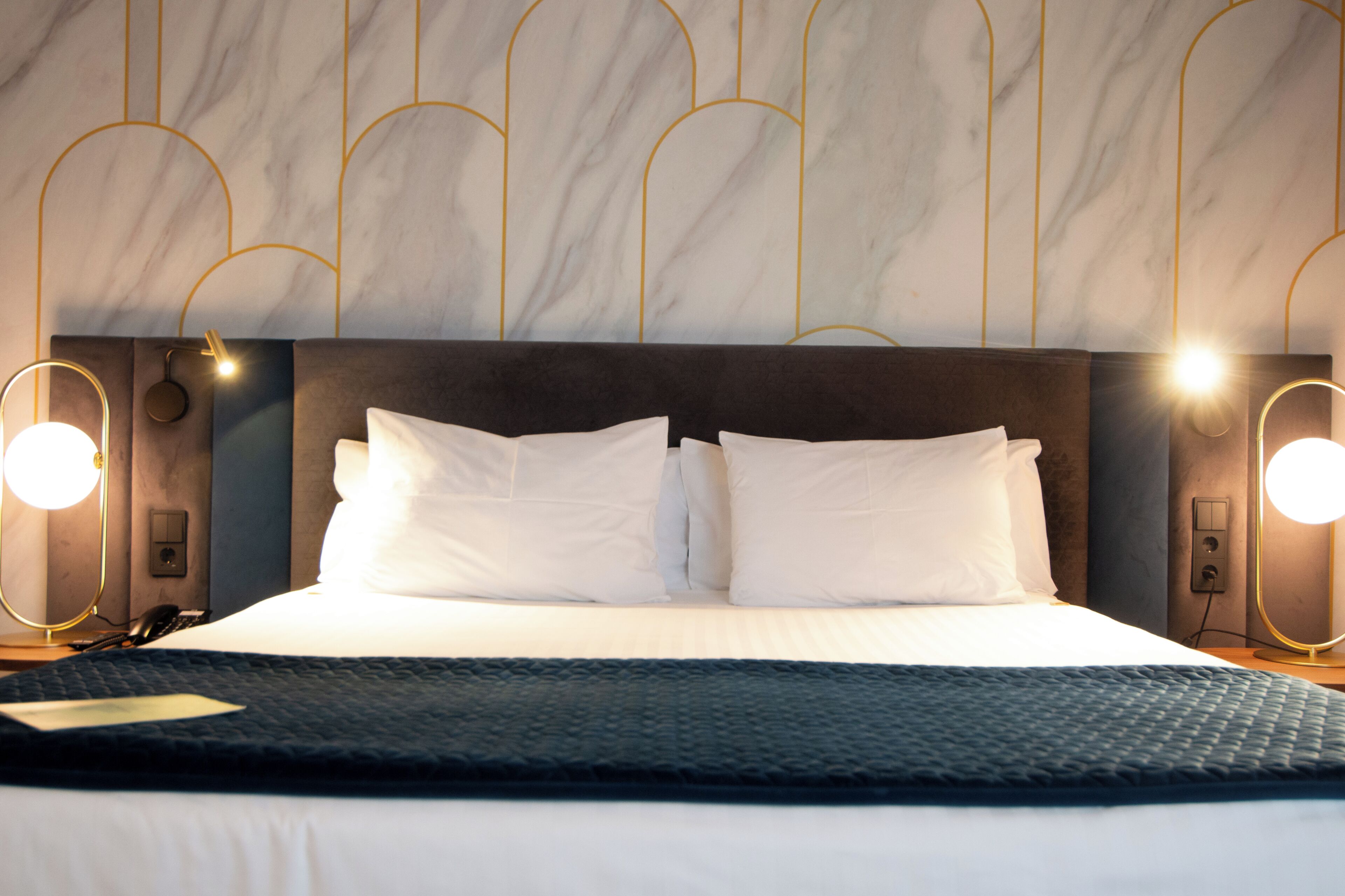 A hotel room with a large bed, two bedside lamps, and a marble-patterned wall.