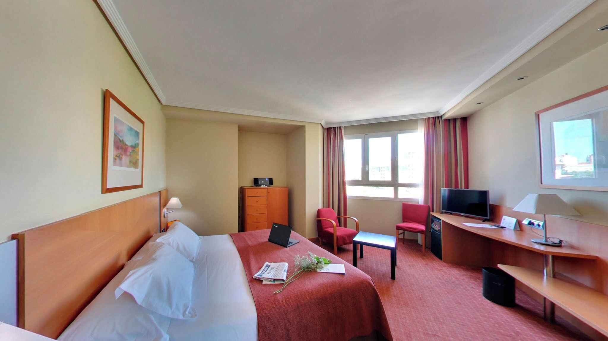 A hotel room with a bed, a desk, a chair, a television, and a window with curtains.