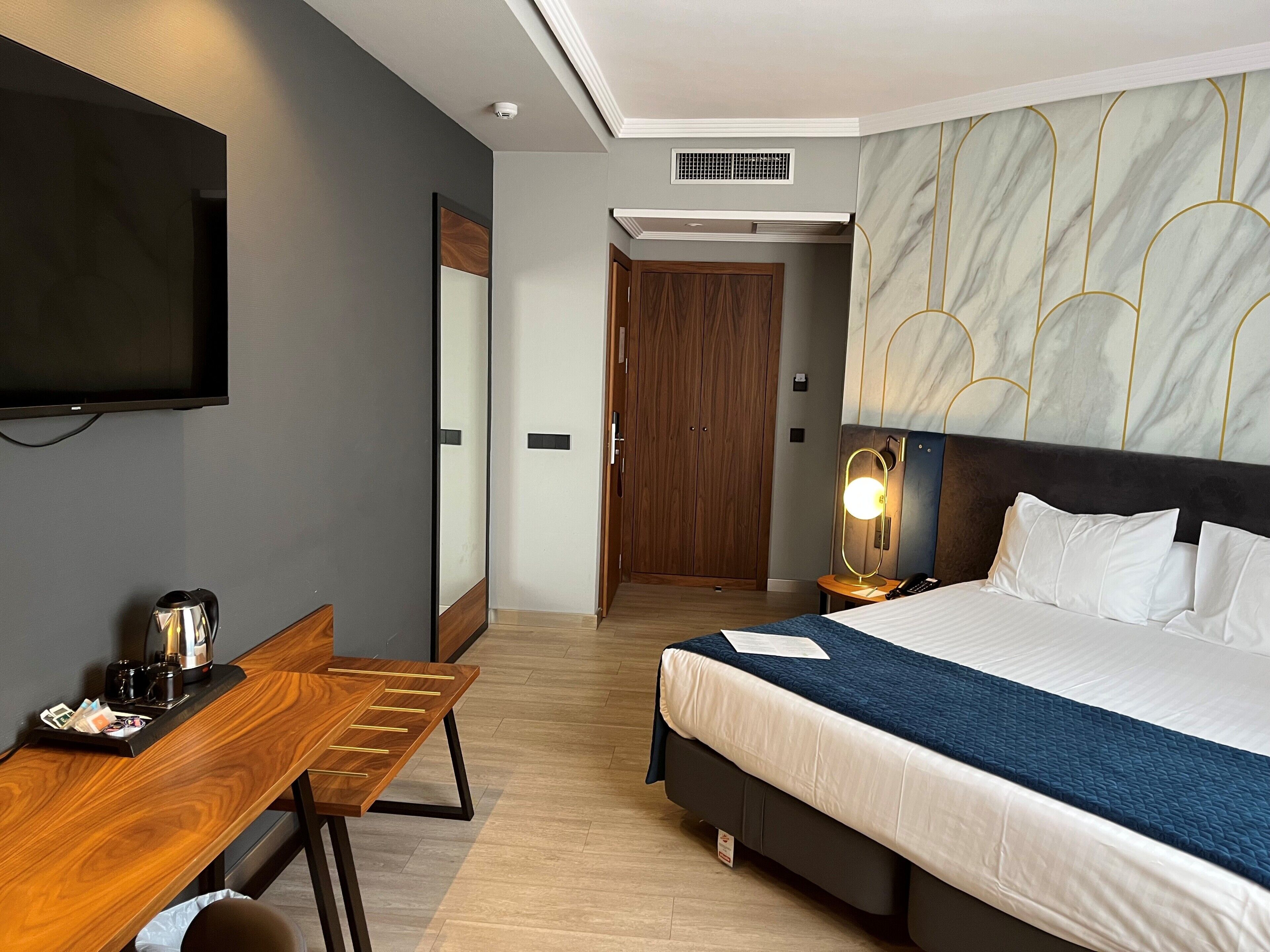 A hotel room with a bed, a desk, a television, and a mirror.