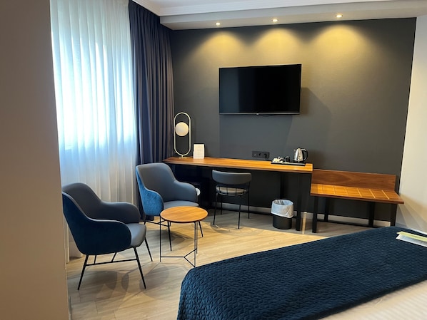 Habitación de hotel con cama, escritorio, dos sillas, televisión y ventana con cortinas.