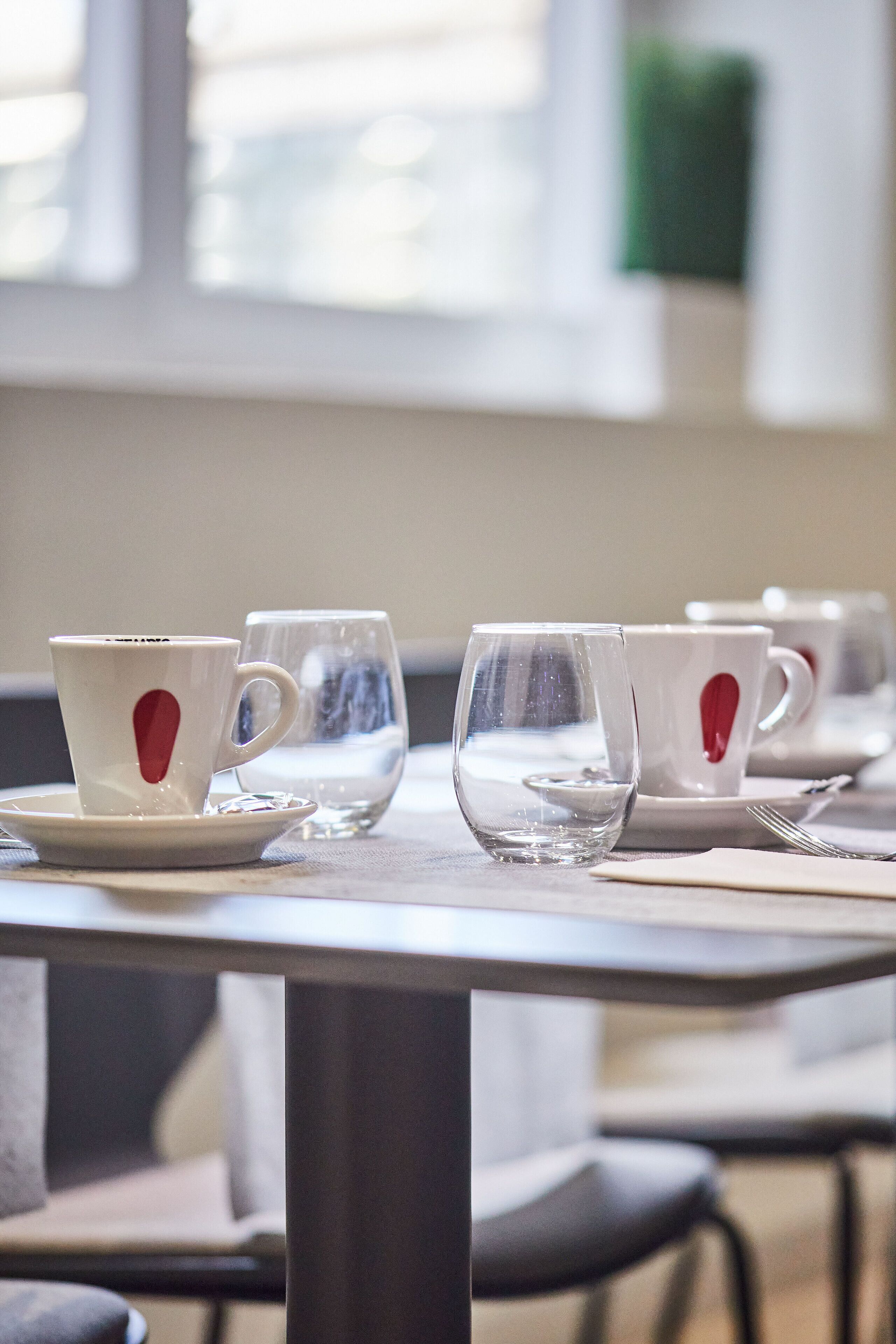 A table with white cups and saucers, some with red designs, and clear glasses.