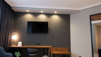 Una sala de estar moderna con un televisor de pantalla plana montado en la pared, un escritorio de madera, una silla, un sofá y una mesita con una planta.