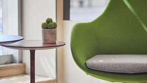 Ein grüner Stuhl mit grauer Sitzkissen, ein kleiner Blumentopf auf einem runden Tisch und ein Holzboden mit einem Muster.