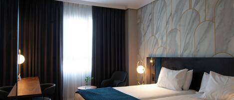 Habitación de hotel con cama, escritorio, silla y un amplio ventanal con cortinas.