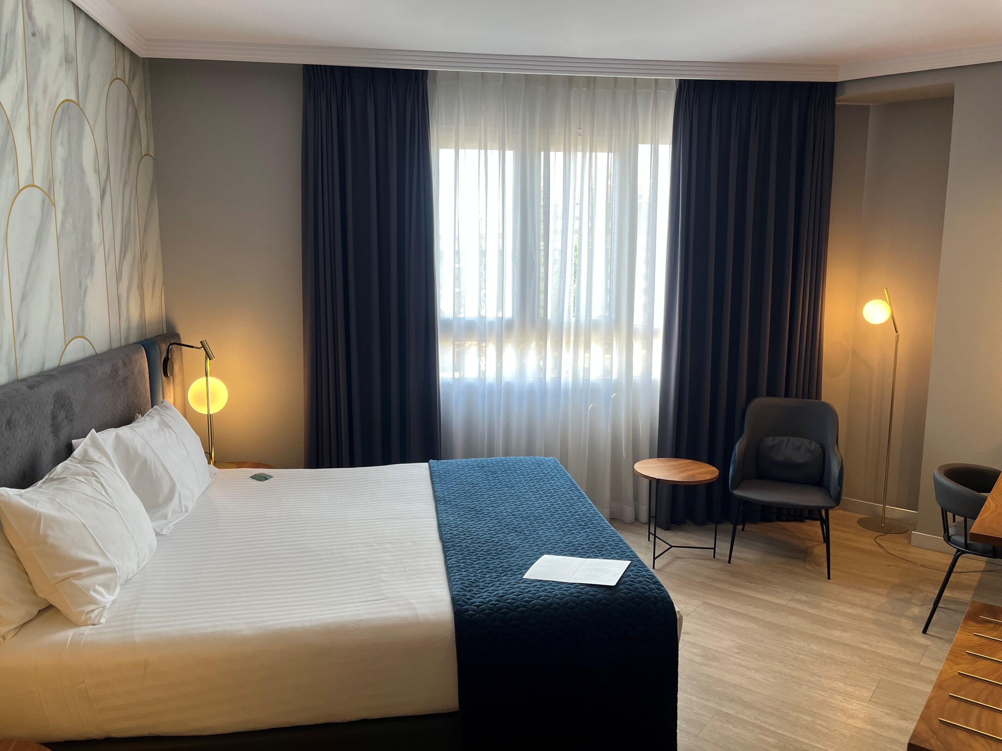 Habitación de hotel con una cama grande, una silla, una mesita y una lámpara de pie.