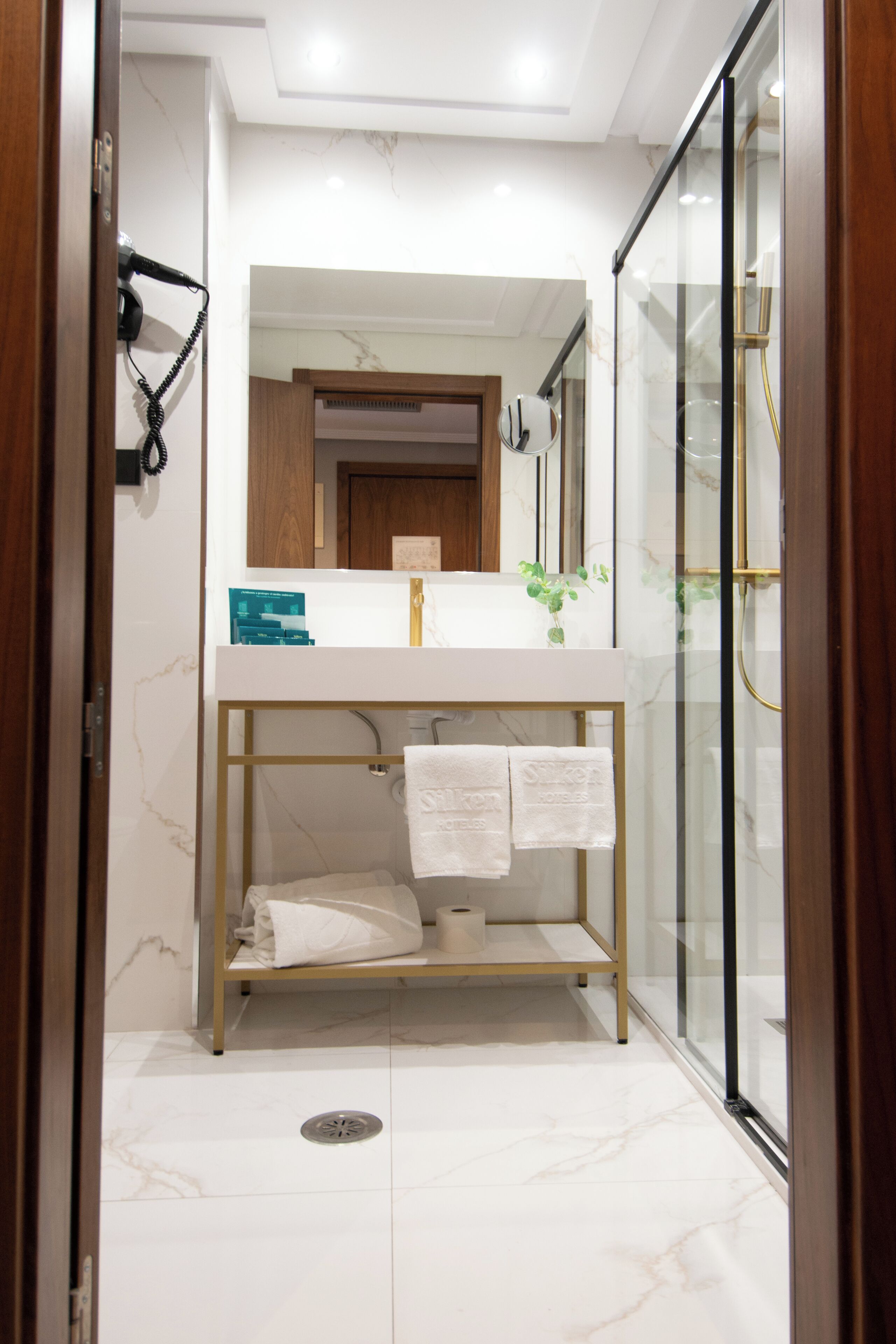 A modern bathroom with a glass shower enclosure, a marble-tiled floor, and a wooden vanity with a mirror above.