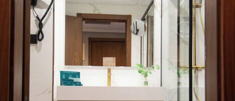 A modern bathroom with a glass shower enclosure, a marble-tiled floor, and a wooden vanity with a mirror above.
