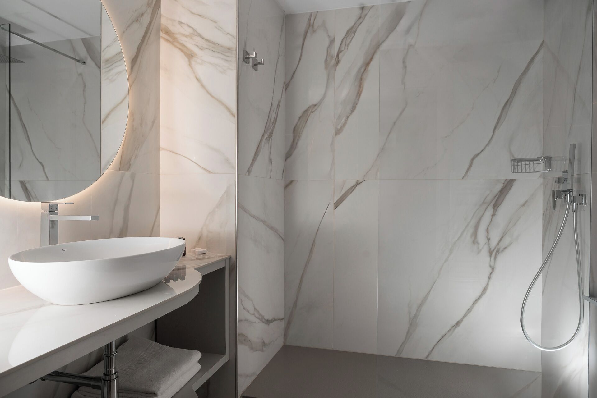 A modern bathroom with a large, oval sink, a glass shower enclosure, and marble-patterned walls.