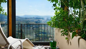 A balcony with a white chair, a glass table, and a view of a valley.