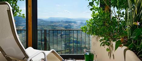 Un balcón con una silla blanca, una mesa de vidrio y vistas a un valle.