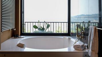 Een moderne badkamer met een ruime badkuip, een raam met uitzicht op zee en een wastafel met spiegel en handdoekhouder.