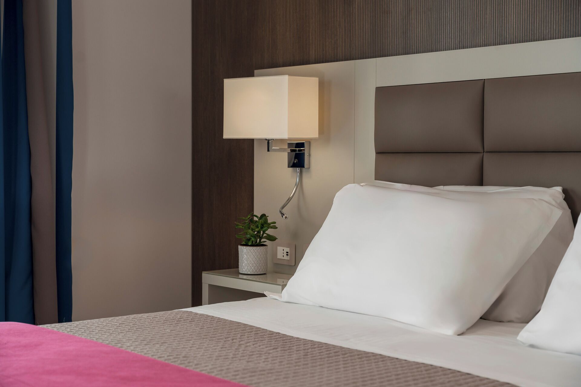 A hotel room with a bed, a nightstand, a lamp, and a potted plant.