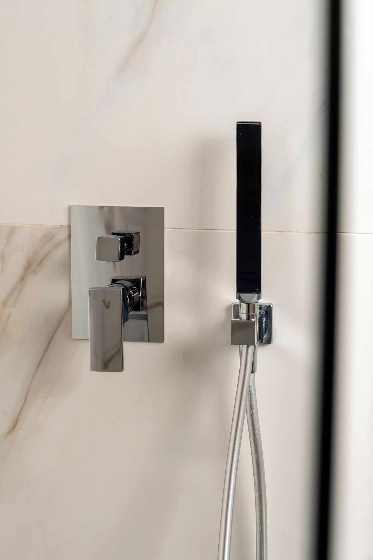 A modern shower with a control panel and a handheld showerhead mounted on a marble wall.
