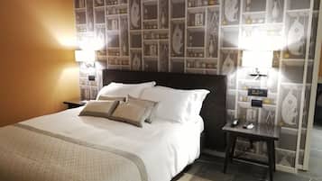 A neatly made bed with white linens and multiple pillows, a bedside table with a lamp, and a wall with a decorative pattern.