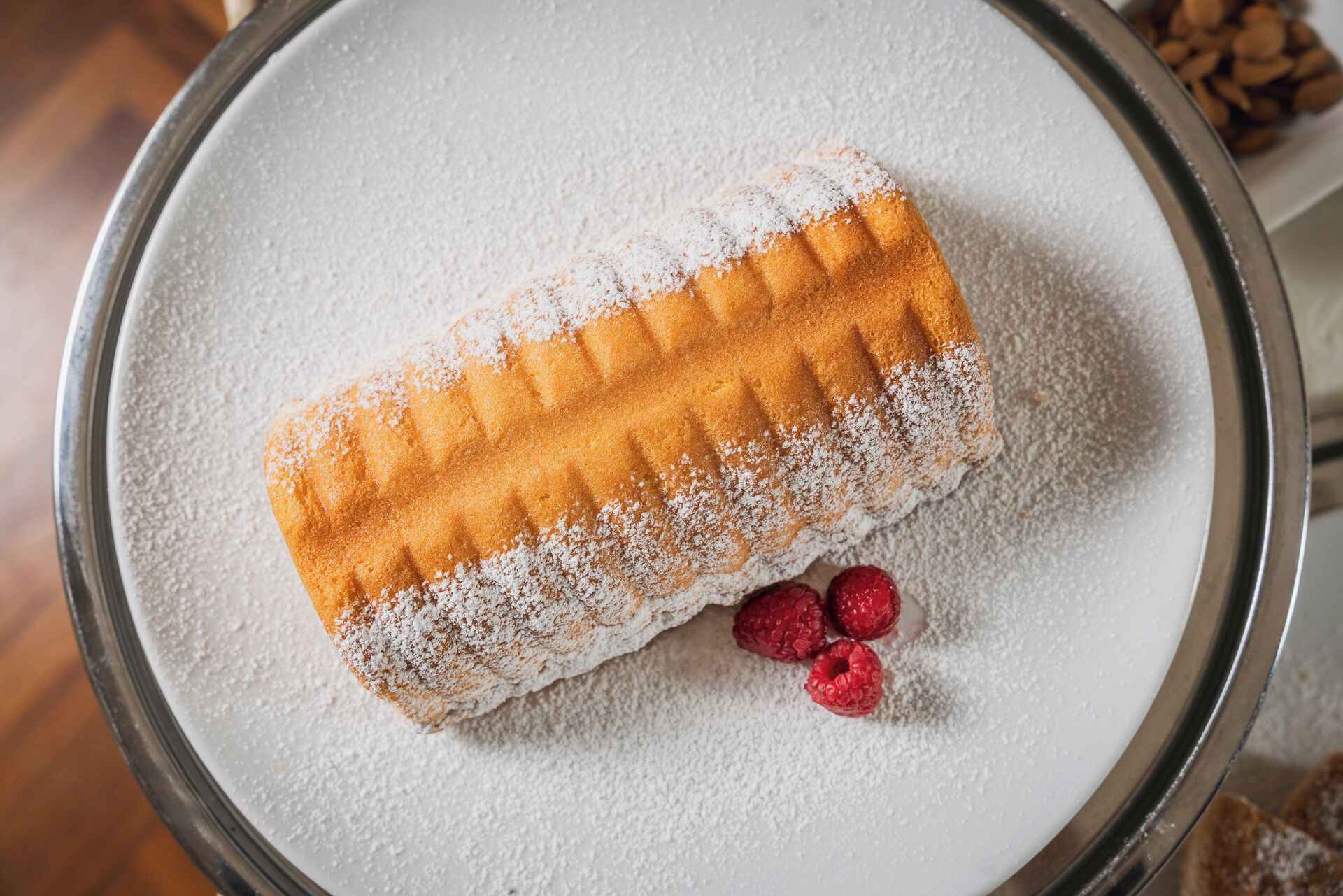 Un gaufre saupoudrée de sucre glace et garnie de framboises, présentée sur une assiette.