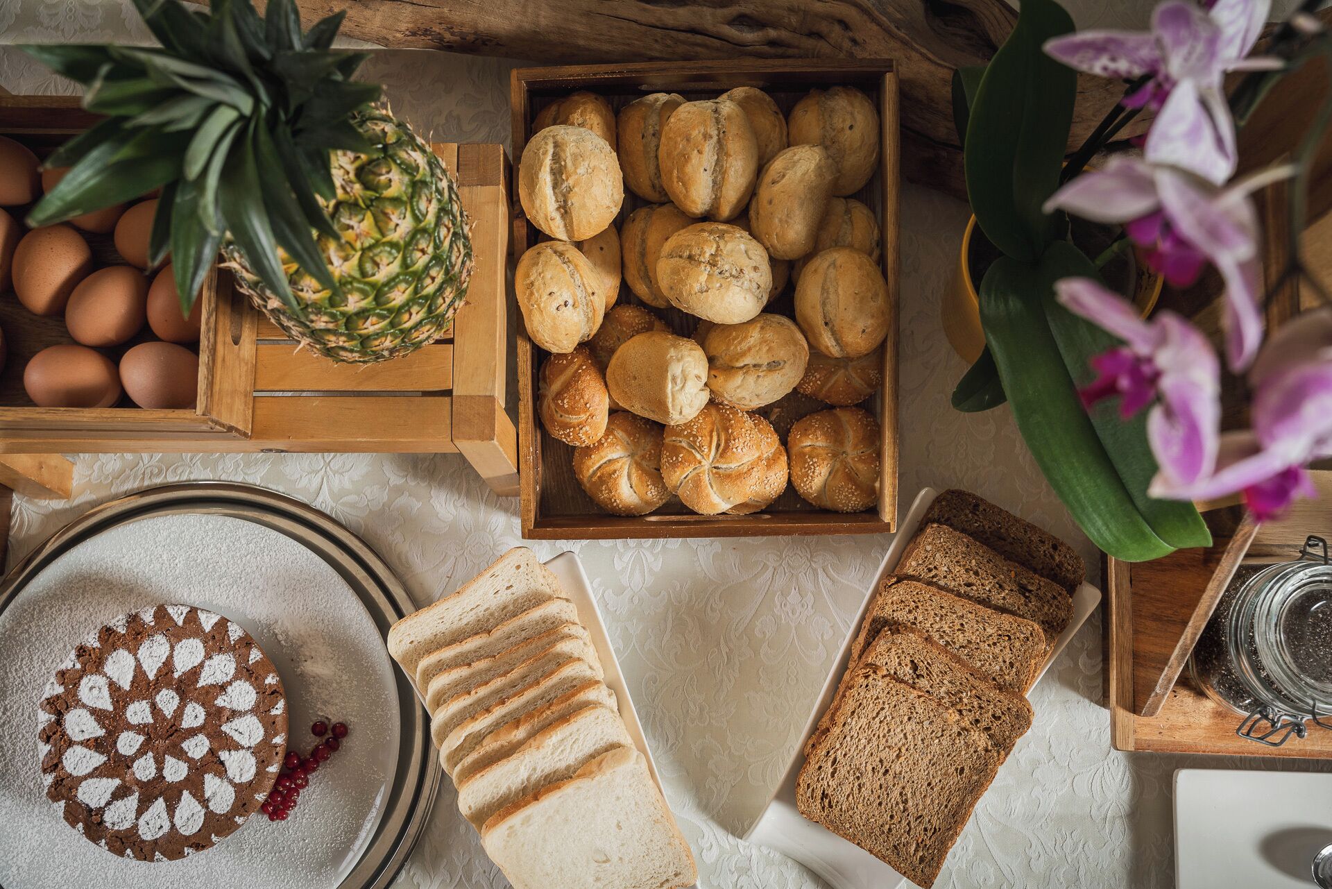 A wooden crate with bread rolls, a pineapple, eggs, and a cake with a white topping.