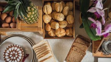 A wooden crate with bread rolls, a pineapple, eggs, and a cake with a white topping.