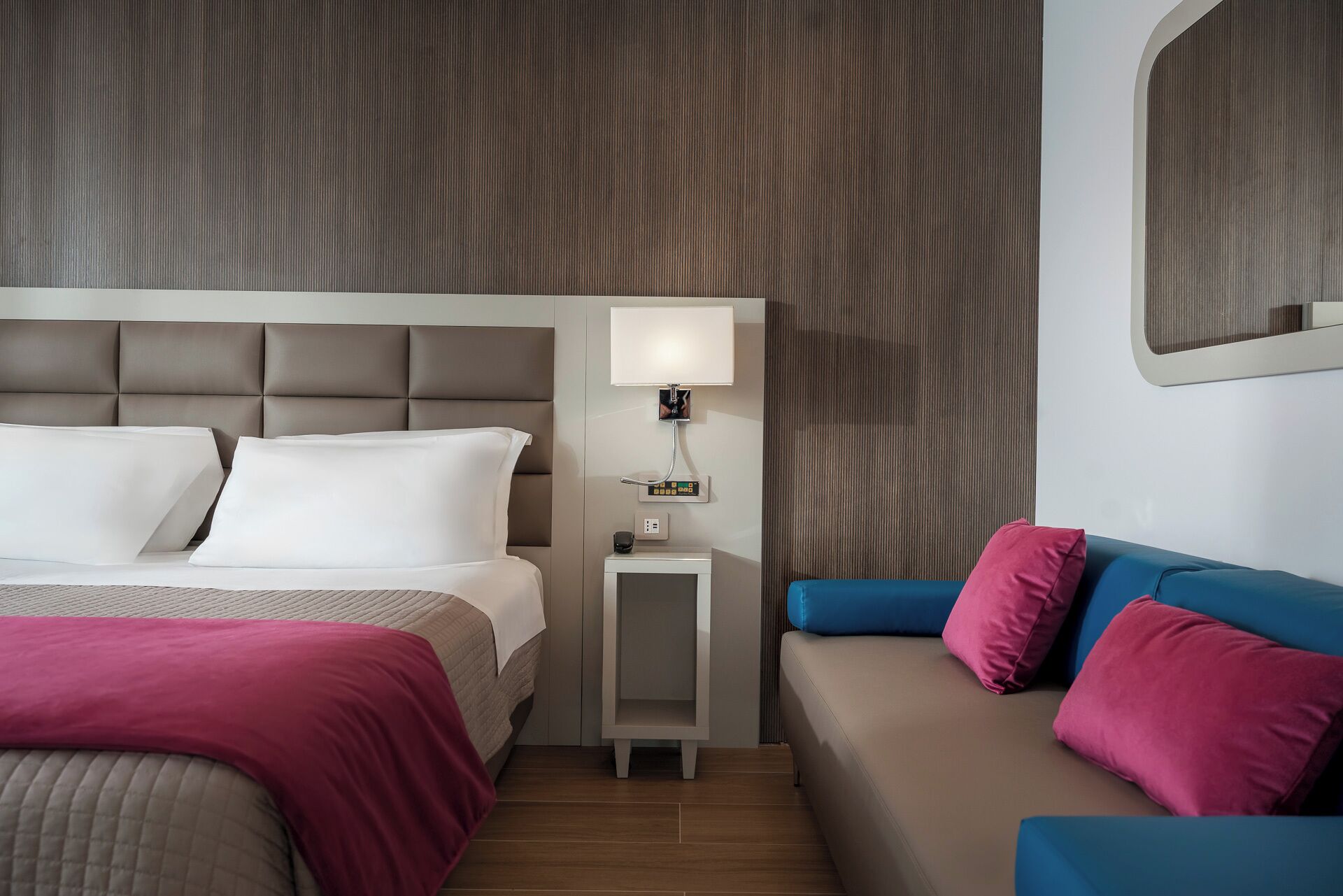 Una habitación de hotel con cama, mesita de noche, lámpara y un sofá.