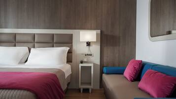 Una habitación de hotel con cama, mesita de noche, lámpara y un sofá.