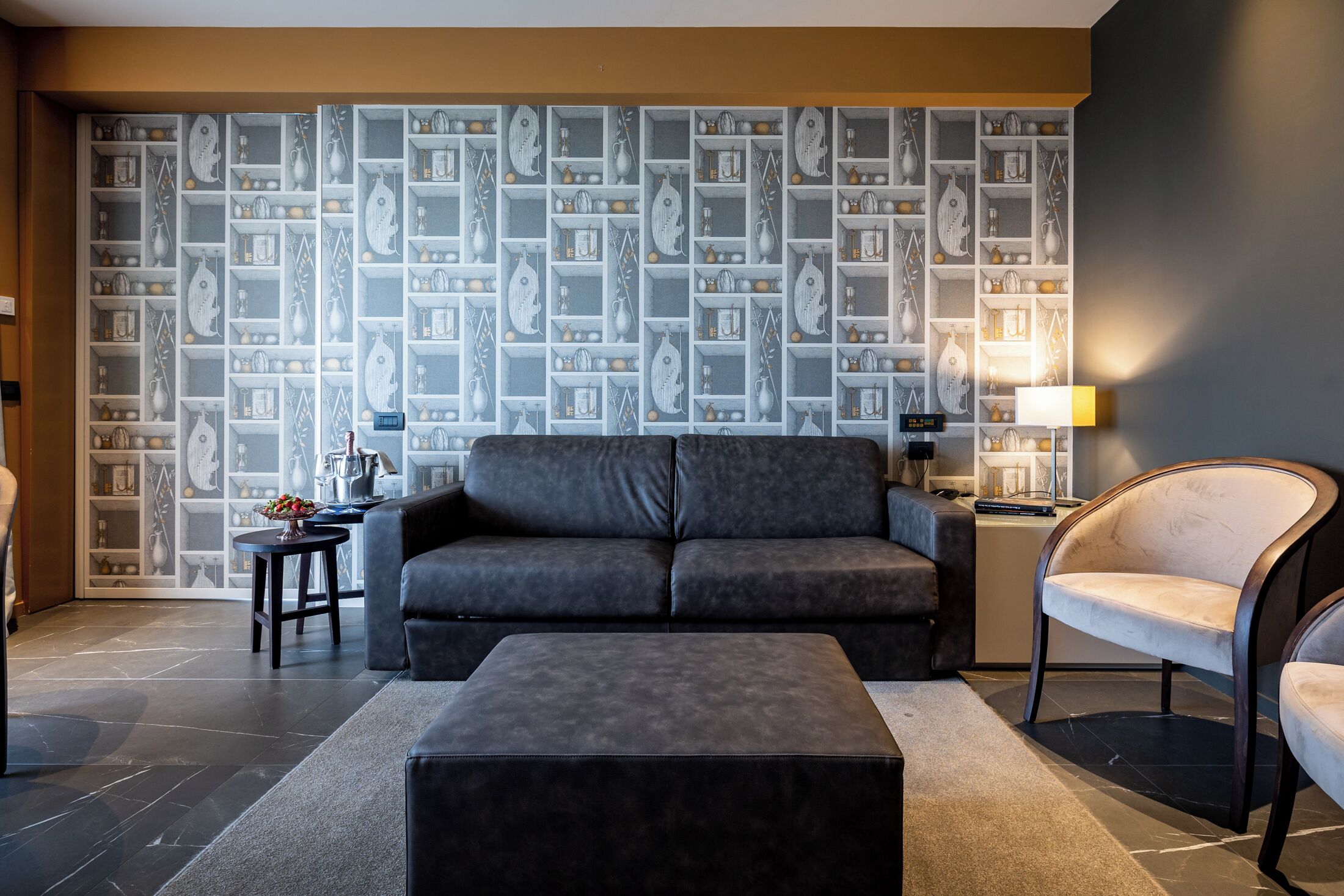 Ein modernes Wohnzimmer mit einem grauen Sofa, einem passenden Hocker und einer Wand mit Muster.