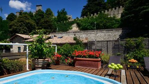 A swimming pool surrounded by a wooden deck, with a stone building and a castle in the background.
