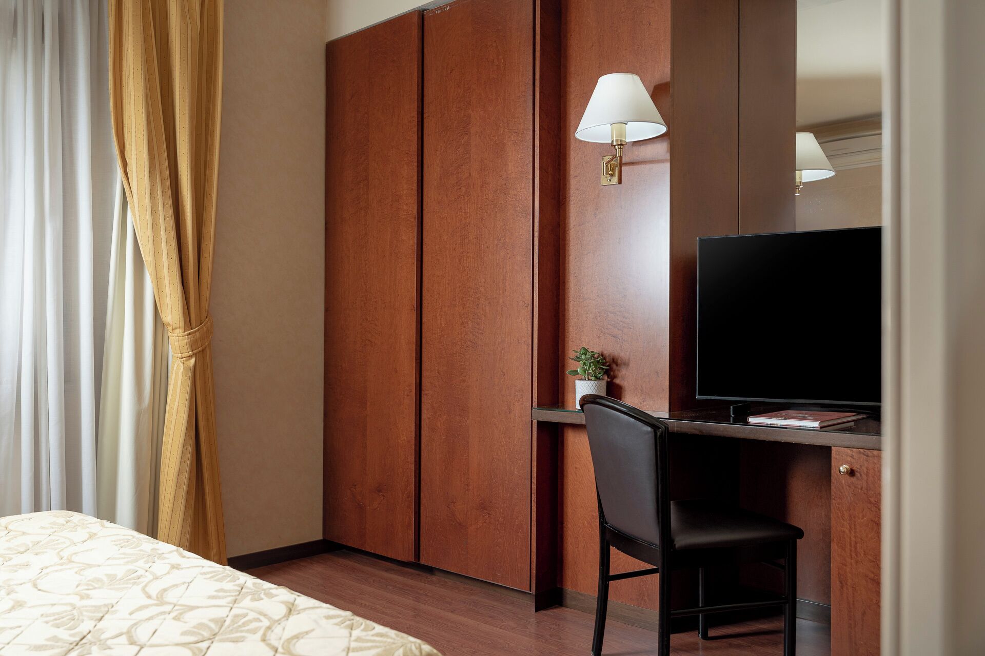 Une chambre d’hôtel comprenant un lit, un bureau avec une chaise, une télévision et une armoire.