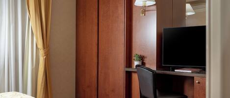 A hotel room with a bed, a desk with a chair, a television, and a wardrobe.