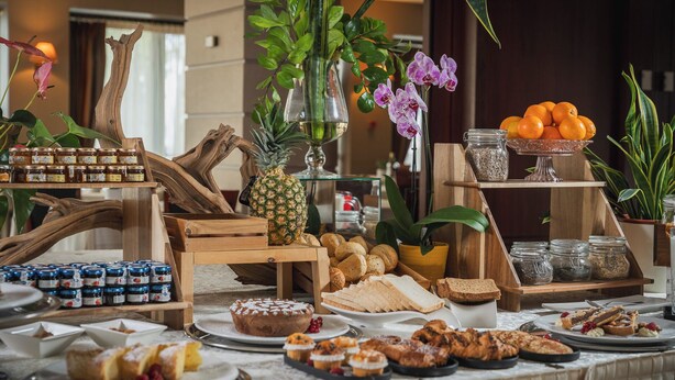 A buffet with various food items, including bread, pastries, and fruits, arranged on a table with a decorative backdrop.