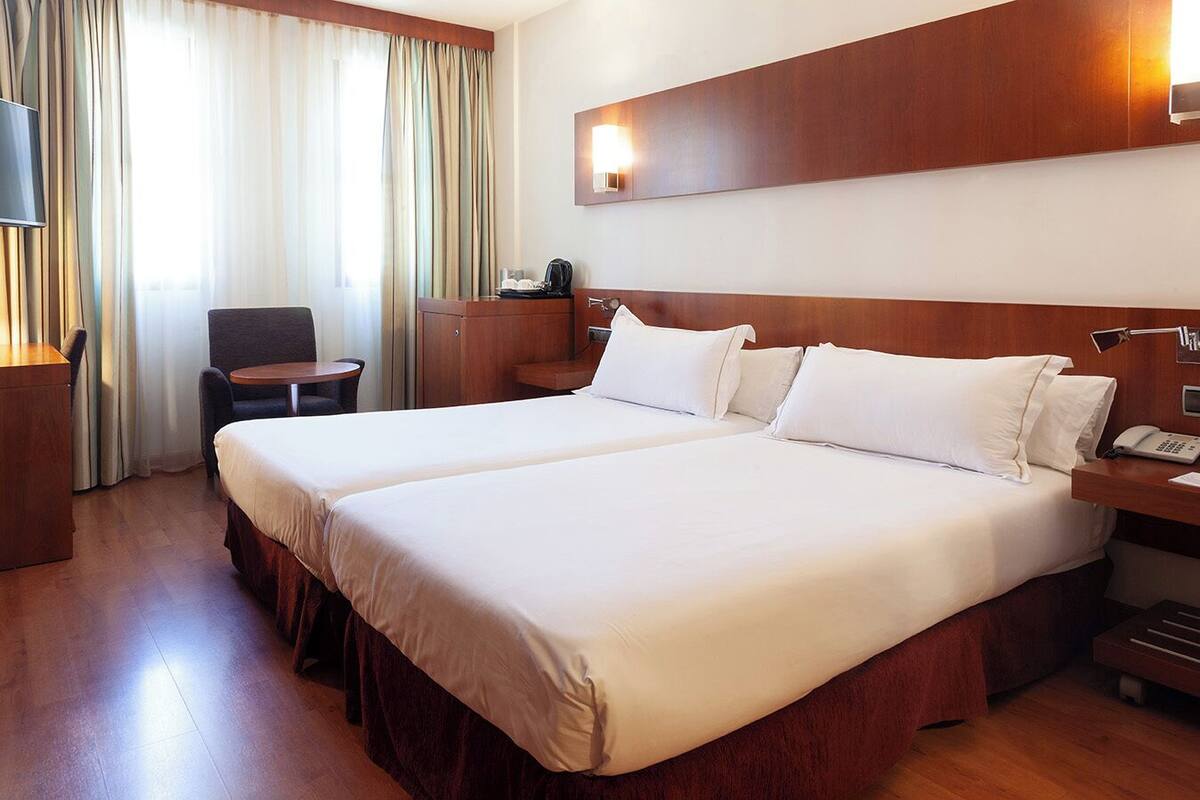 A hotel room with a large bed, a desk, a chair, and a desk lamp.