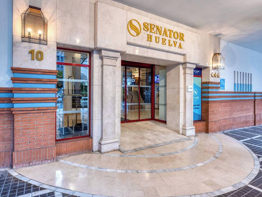 The exterior of the Senator Huelva hotel with a prominent entrance, numbered 10, and a tiled plaza area.