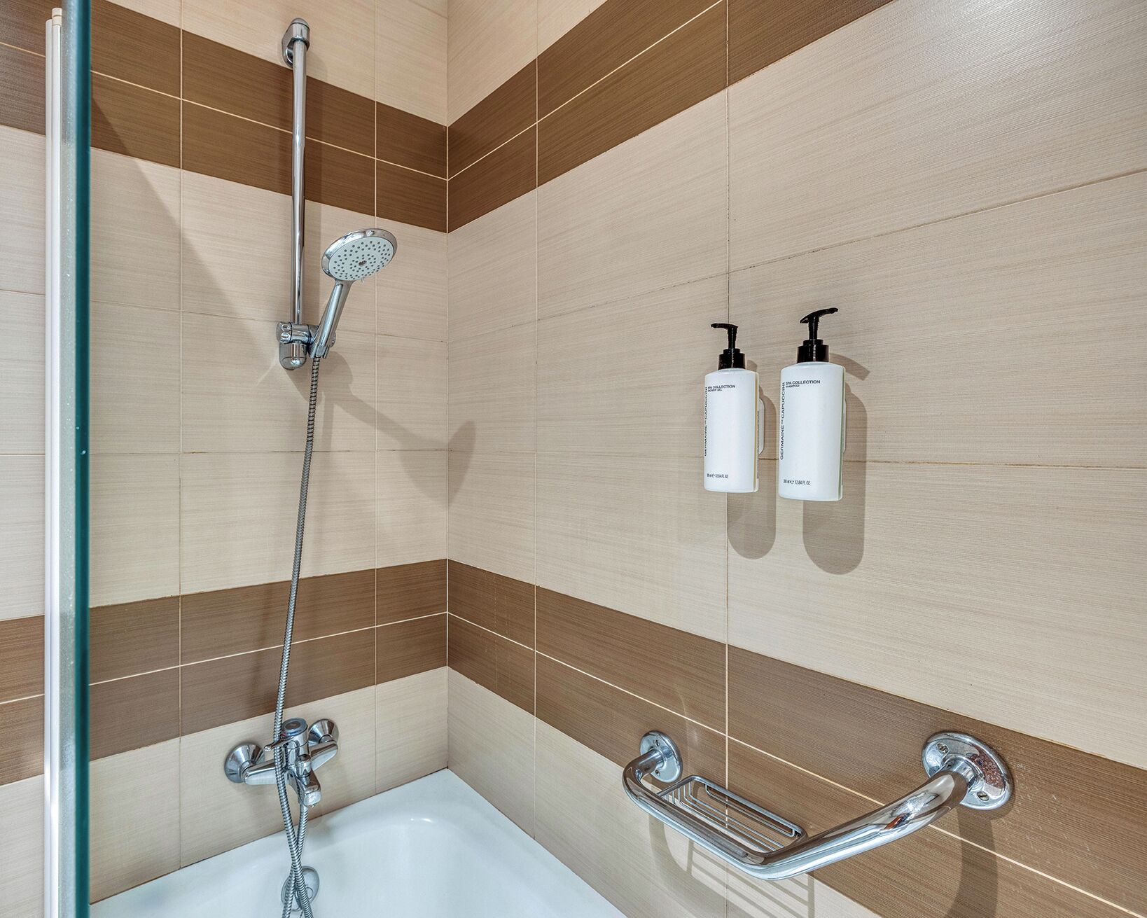 A bathroom with a shower, a bathtub, and two toiletry bottles mounted on the wall.