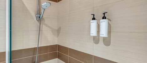 Un baño con ducha, bañera y dos botellas de artículos de aseo personal fijadas a la pared.